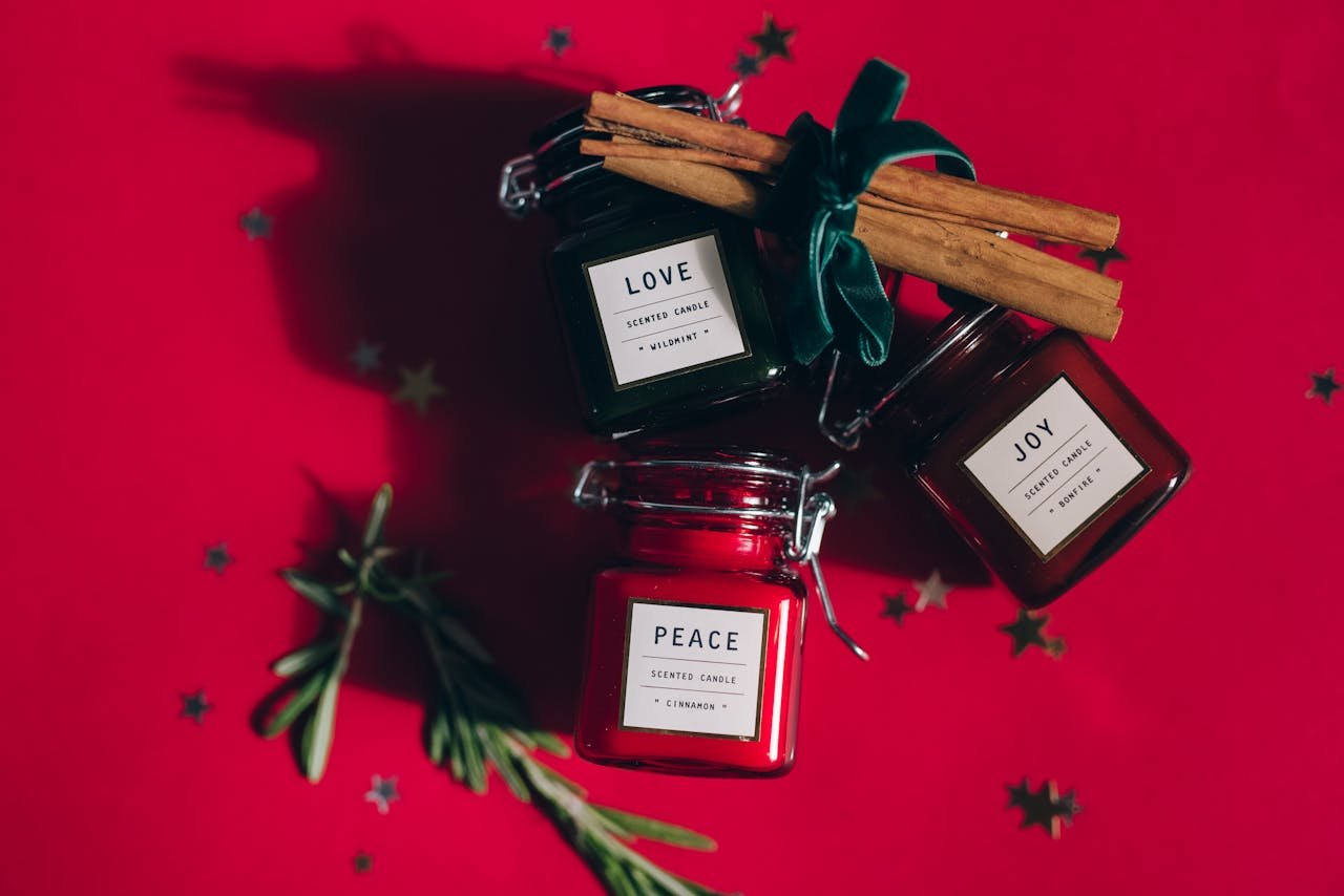 Three festive scented candles labeled Love, Peace, and Joy with cinnamon and rosemary on a red background.